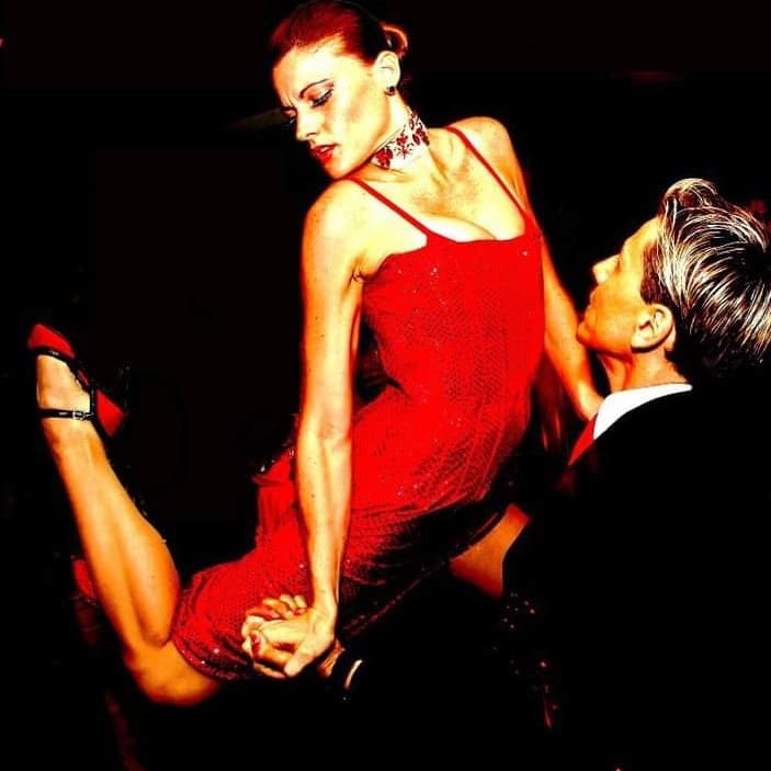 Woman in red dress performs a dramatic high-kick tango pose with a male partner.