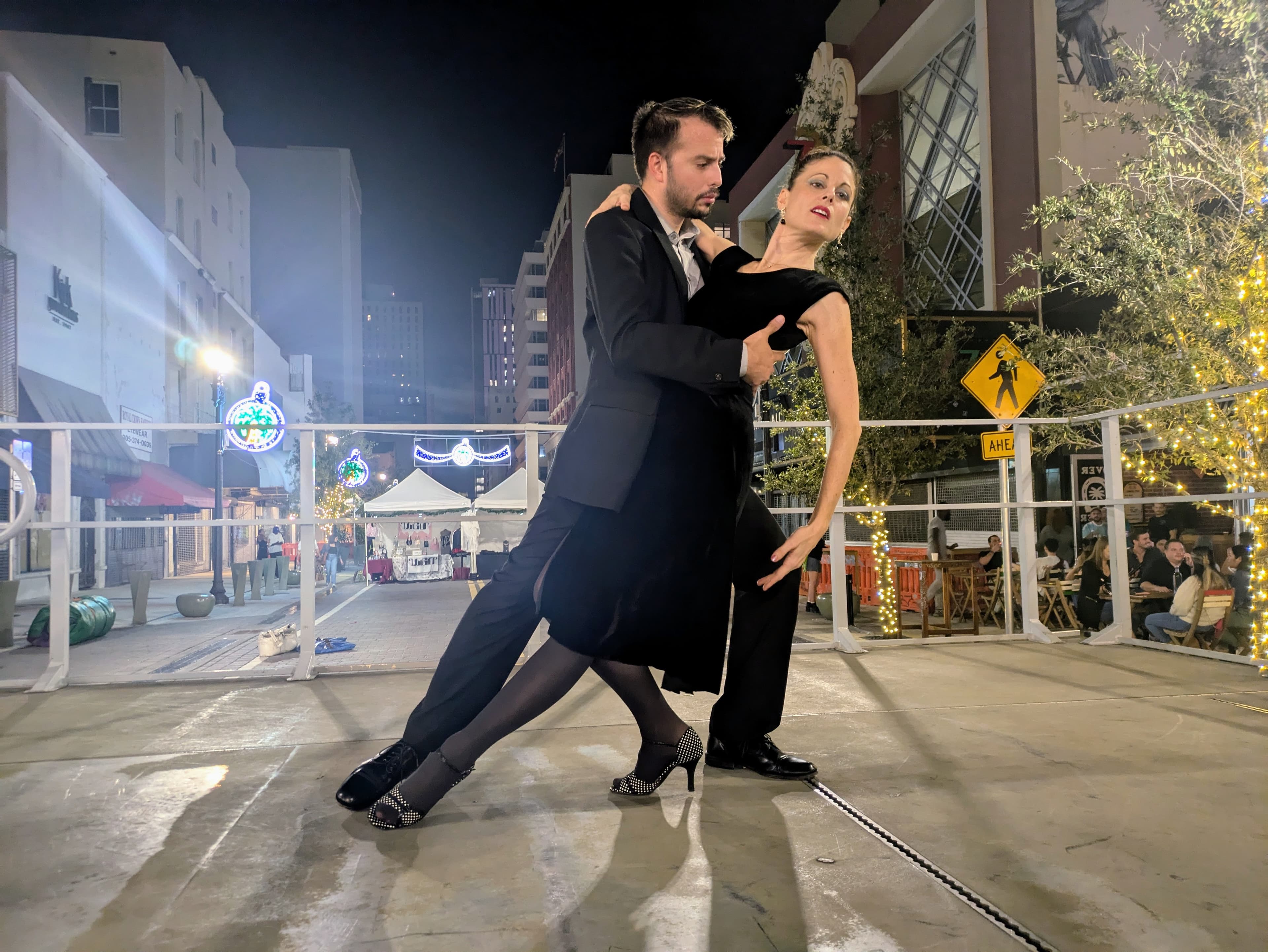 A couple performs a dramatic tango dance on an outdoor city stage at night.